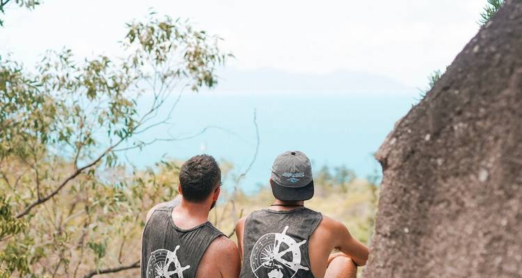 Deux randonneurs se reposant sur un point de vue rocheux contemplant l'océan bleu et les îles lointaines.