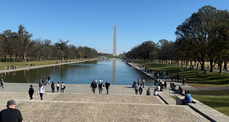 Large promenade bordant le bassin aux reflets avec des visiteurs regardant vers le distant Monument de Washington.