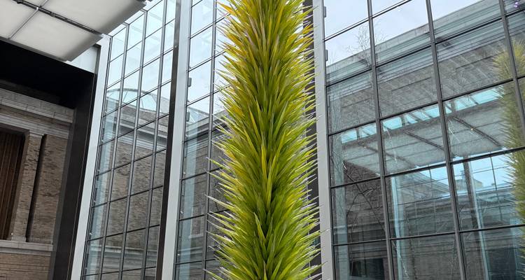 Une imposante sculpture en verre vert citron s'élève vers un puits de lumière à l'intérieur d'un atrium moderne.