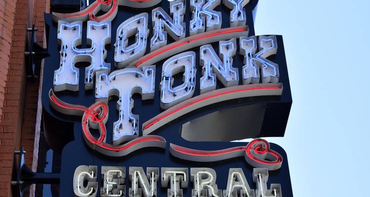 Retro-Neonschrift mit der Aufschrift "Honky Tonk Central" an einer Backsteinmauer vor blauem Himmel angebracht.