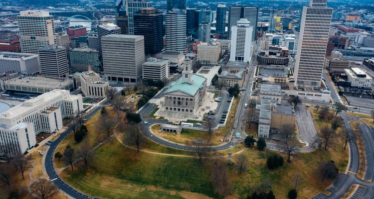 Vista aérea del Capitolio Estatal de Tennessee rodeado de rascacielos del centro de Nashville y carreteras curvas.