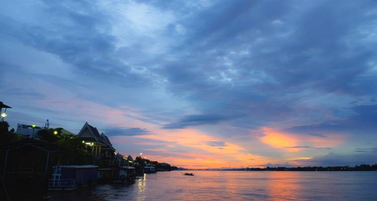 Atardecer colorido sobre un río ancho con casas ribereñas y botes silueteados