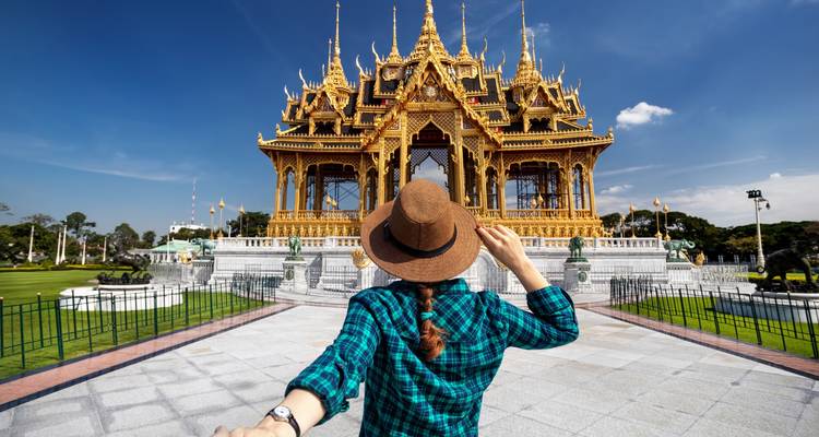 Viajera con sombrero observando un templo dorado y ornamentado bajo un cielo azul brillante