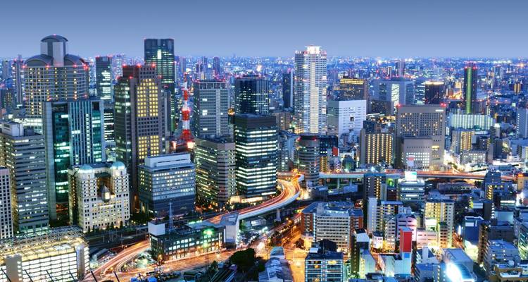 Amplio paisaje nocturno de la ciudad de Osaka con rascacielos brillantes y senderos de luz sinuosos del tráfico.