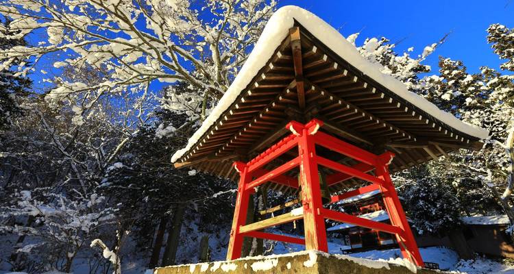 Pabellón de campana de santuario rojo cubierto de nieve con cielos azules brillantes de invierno en las montañas.