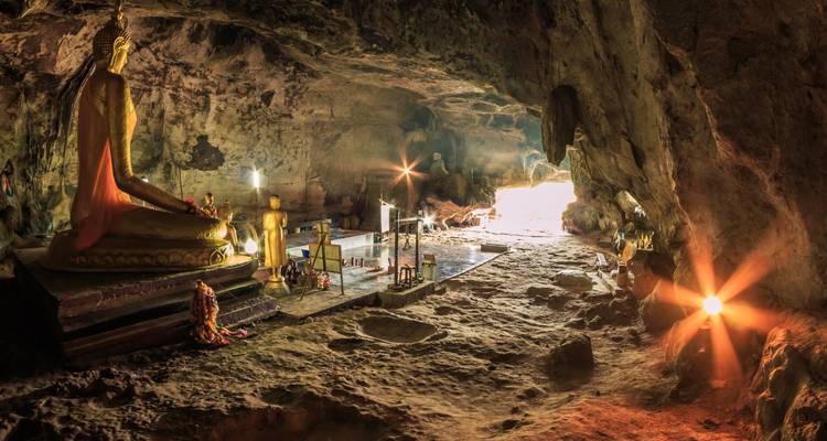 Sanctuaire de grotte faiblement éclairé avec des statues de Bouddha dorées et des rayons de lumière s'écoulant vers l'entrée.