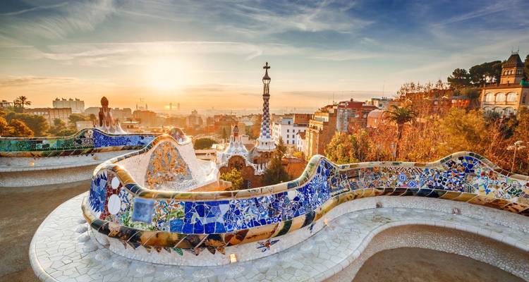 Bancos de mosaico colorido del Parque Güell con vistas a Barcelona al amanecer con un cielo cálido.