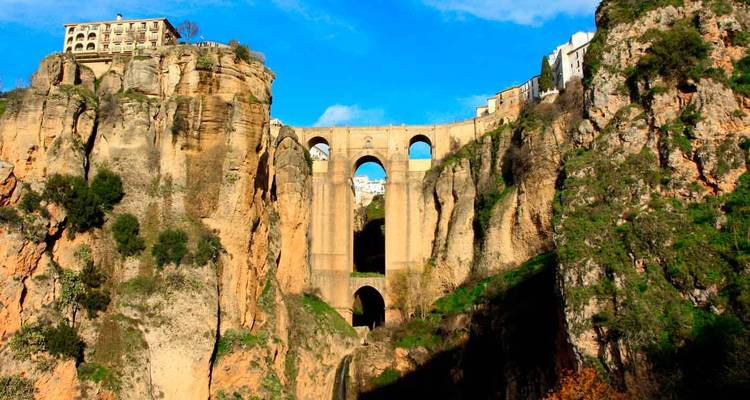 Le spectaculaire pont en pierre Puente Nuevo enjambe une gorge rocheuse profonde sous un ciel bleu éclatant.