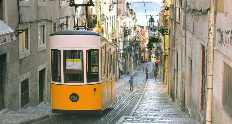 Tramway funiculaire jaune historique montant une rue pavée de galets escarpée bordée de bâtiments anciens à Lisbonne.