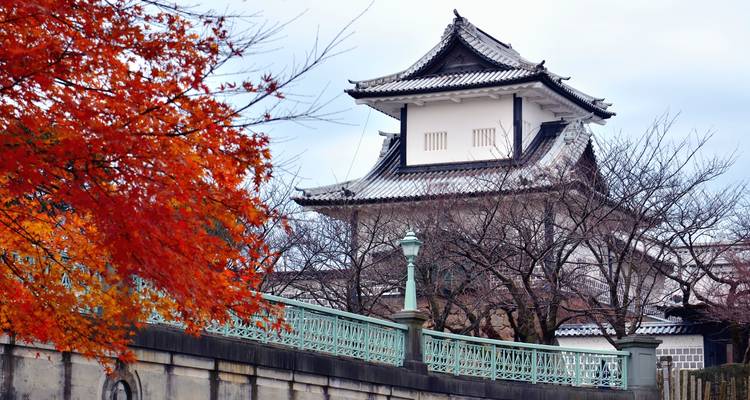 Castle turret framed by vivid autumn maple leaves and decorative bridge railings.