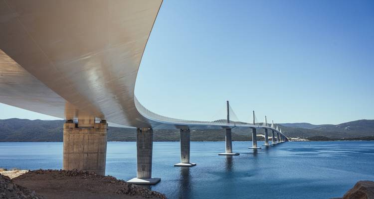 Elegante Pelješac-Brücke, die sich an einem klaren Tag über das leuchtend blaue Wasser der Adria wölbt.