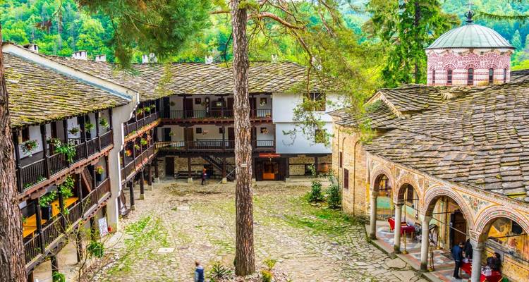Stiller Steinhof eines historischen Klosterkomplexes mit gewölbten Säulenhallen und hölzernen Balkonen inmitten hoher Kiefern