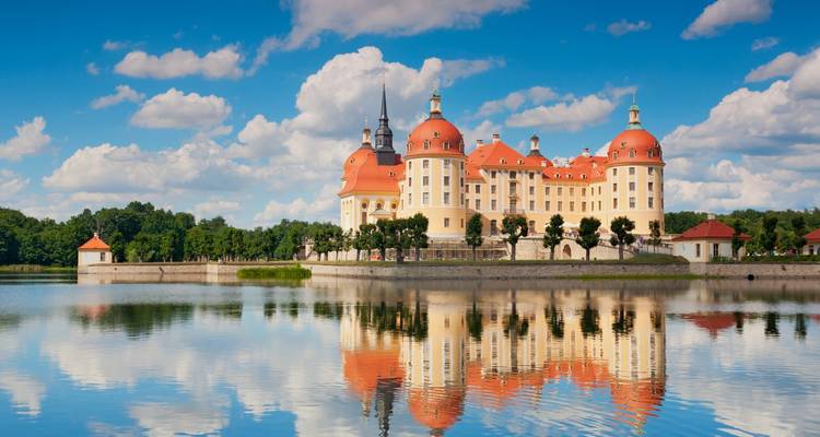 Le magnifique château baroque de Moritzburg aux dômes orange se reflétant parfaitement dans un lac calme sous un ciel bleu éclatant.
