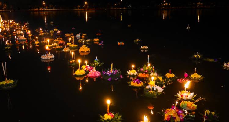 Des dizaines de radeaux floraux illuminés par des bougies flottant sur des eaux sombres lors du festival Loy Krathong la nuit