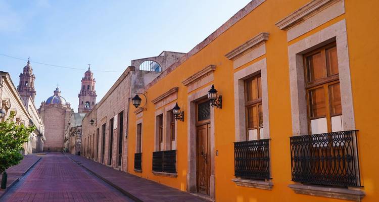 Farbenfrohe Kolonialstraße in Morelia mit leuchtend gelben Fassaden, die zu den Domtürmen in der Ferne führen.