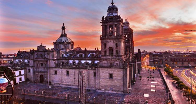 Dramatischer Sonnenuntergang über der Metropolitankathedrale von Mexiko-Stadt mit lebendigen Farben, die den Himmel und die Straßen beleuchten.