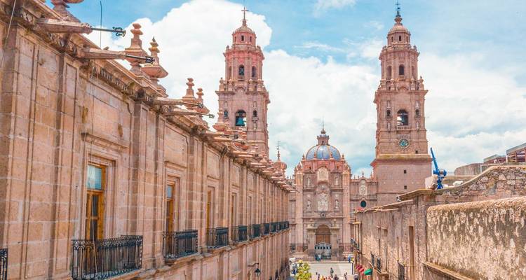 Historische Steingebäude und Doppeltürme der Kathedrale von Morelia vor einem blauen Himmel mit leichten Wolken.