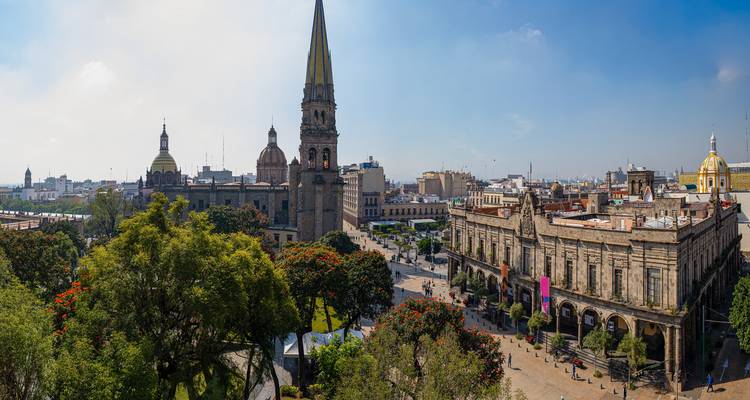 Panoramic view over Guadalajara's historic center with cathedral spire and leafy plaza.