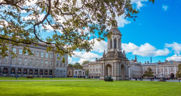 Weitläufiger Rasen des Trinity College Dublin mit seinem Glockenturm, umrahmt von Steingebäuden und einem strahlend blauen Himmel.