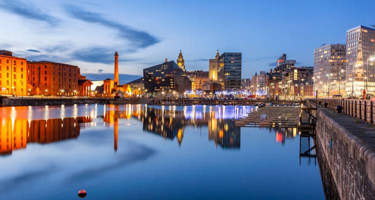 Nächtliche Uferpromenade von Liverpool mit moderner Skyline und Lichtern der Albert Dock, die sich im ruhigen Wasser spiegeln.