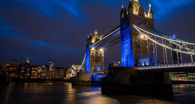 Tower Bridge in Londen verlicht met blauwe lichten boven de rivier de Theems 's nachts met stadslichten die op het water weerspiegelen.