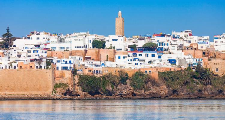 Witgekalkte huizen en een hoge minaret bovenop oude vestingwerken die uitkijken over kalm rivierwater in Rabat.
