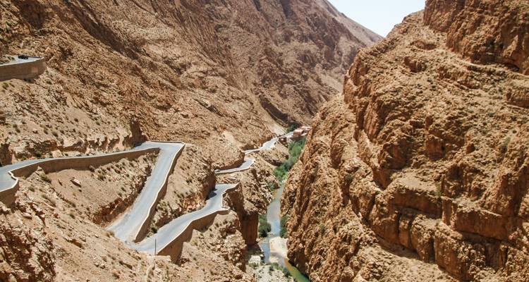 Route de montagne sinueuse creusée dans les parois abruptes d'un canyon de couleur beige au-dessus d'une rivière étroite.