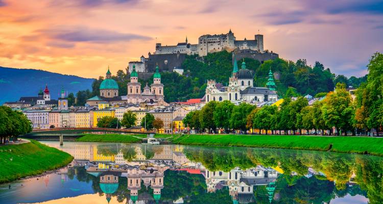 Die farbenfrohe barocke Silhouette von Salzburg spiegelt sich bei Sonnenuntergang perfekt in der Salzach wider.