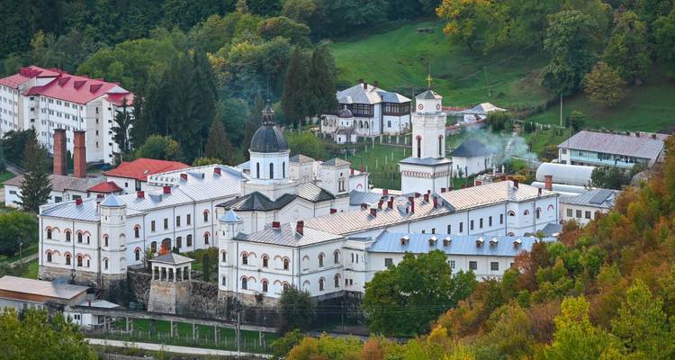 Large hilltop monastery complex surrounded by autumn foliage in the Romanian countryside.