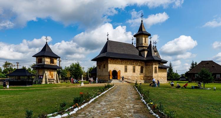 Orthodox wooden church complex with visitors walking the stone path on a bright day.