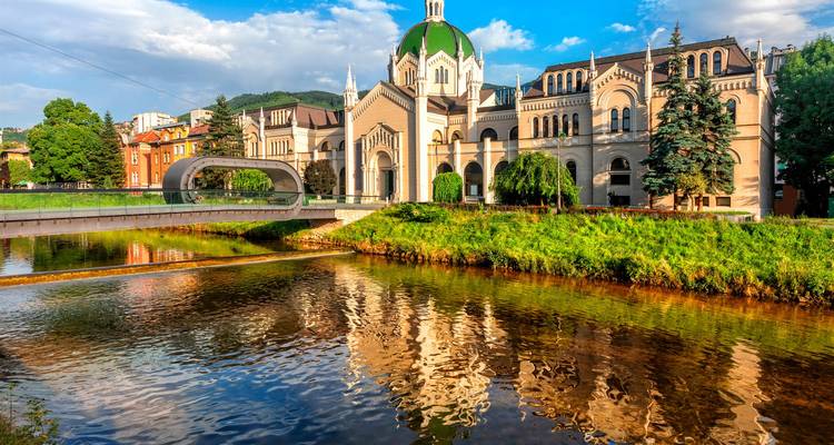 Die grünkuppelige Akademie der Schönen Künste spiegelt sich im Fluss Miljacka mit einer modernen Fußgängerbrücke in Sarajevo.