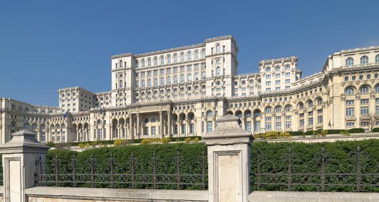 Der massive Palast des Parlamentes in Bukarest erhebt sich hinter gepflegten Hecken unter einem klaren Himmel.
