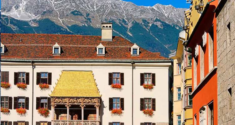 Bâtiment historique du Toit d'Or à Innsbruck encadré par des façades colorées avec les Alpes enneigées s'élevant abruptement derrière.