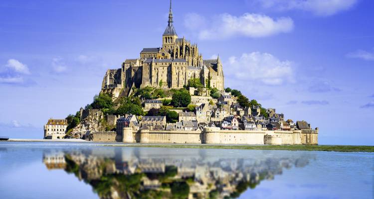 La icónica abadía de Mont Saint-Michel elevándose sobre una bahía de mareas espejada bajo la brillante luz de la mañana