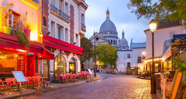 Brillo del atardecer sobre los cafés de Montmartre con la basílica del Sacré-Cœur elevándose detrás de la calle empedrada