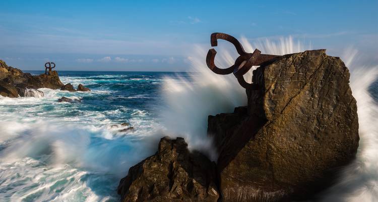 Krachtige oceaangolven die tegen het Peine del Viento-beeldhouwwerk slaan dat in kustrotsen is ingebed.