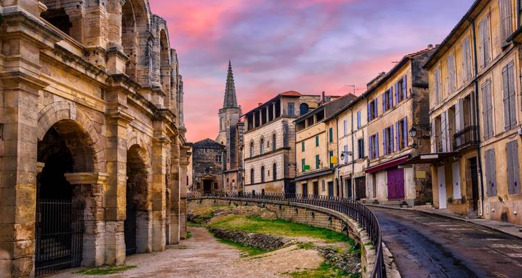 Historische Straßen von Arles bei Sonnenuntergang mit dem römischen Amphitheater und farbenfrohen alten Häusern.