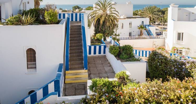 Weiß getünchte Gebäude im mediterranen Stil mit blau gestreiften Akzenten und Treppen mit Blick auf die Atlantikküste in Asilah.