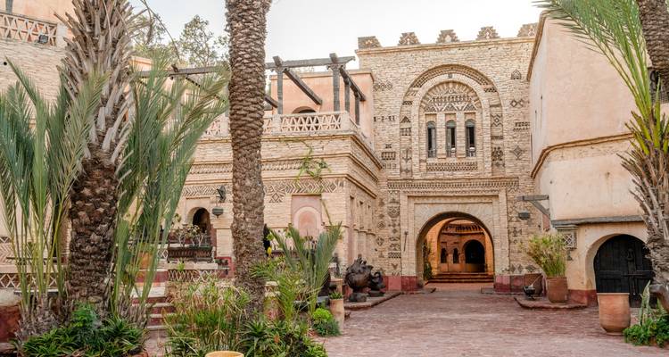 Historisches Steintor und Arkaden, umrahmt von hohen Palmen und üppigen Blumenkübeln in einem traditionellen Riad-Komplex.