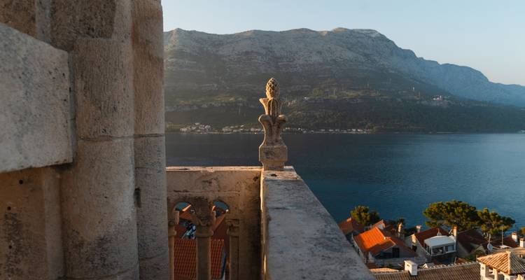 Balustrade eines steinernen Glockenturms mit Blick auf den tiefblauen Kanal und die terrakottafarbenen Dächer von Korčula.