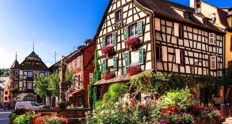 Charming half-timbered house adorned with flowers in a sunny Alsatian village street.