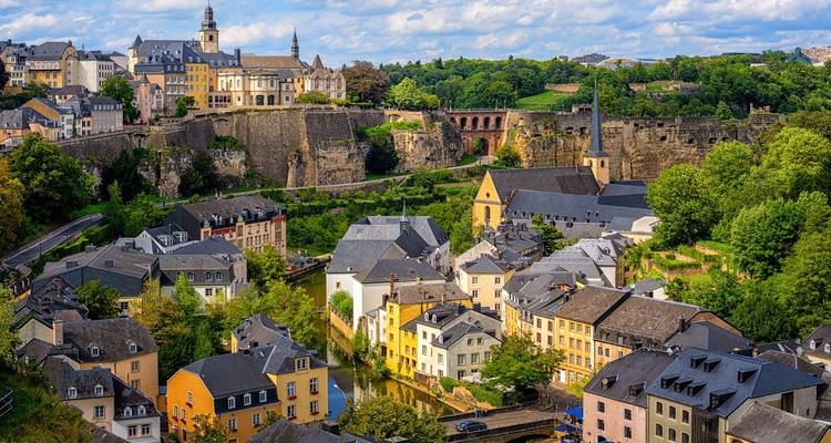 Daylight view over pastel houses and stone fortifications of a historic European valley city.