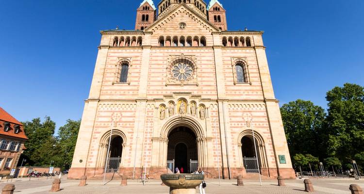 Grand Romanesque cathedral facade with striped stone patterns under a clear blue sky.