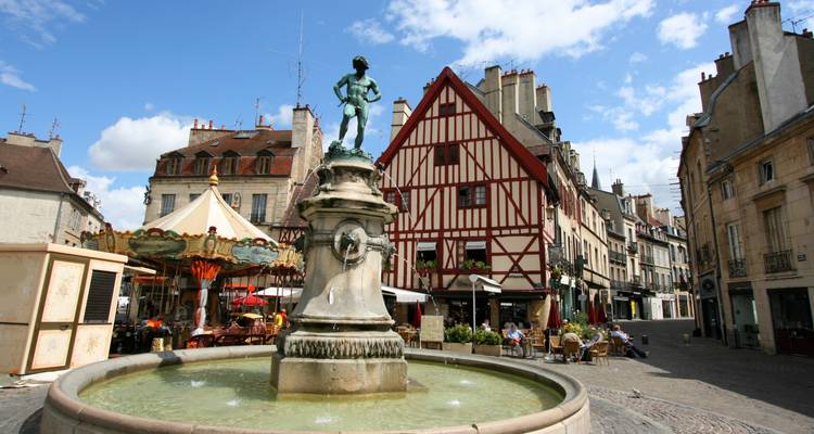 Central fountain with bronze statue in a lively medieval square surrounded by half-timbered buildings.