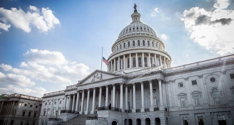 Iconic United States Capitol building onder een heldere lucht met verspreide wolken en een Amerikaanse vlag die wappert.