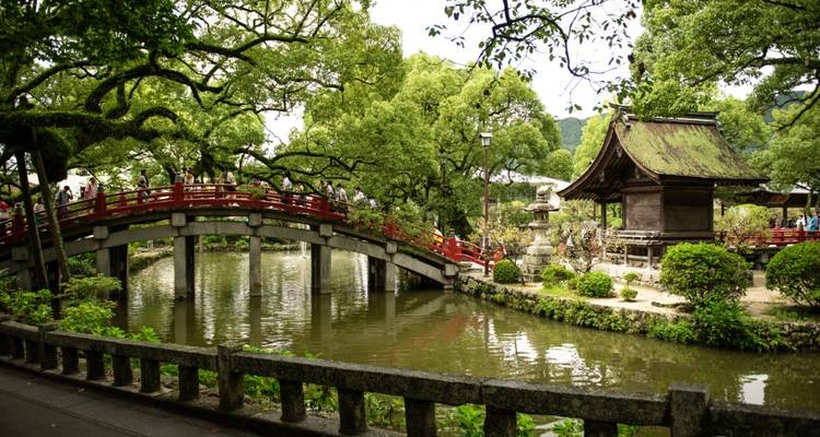 Picturesque red arched bridge crossing a pond amid lush greenery at a traditional shrine garden.