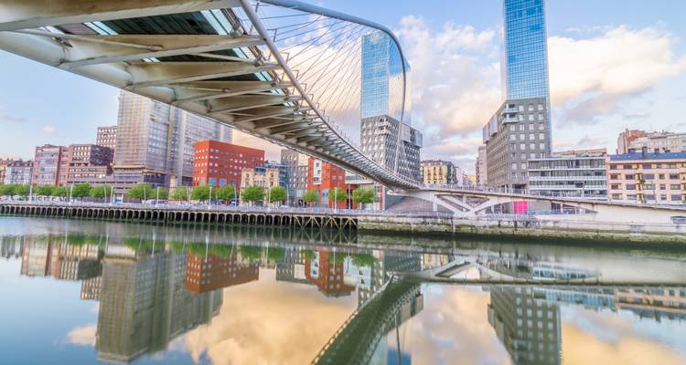 Le pont piétonnier Zubizuri aux arches modernes se reflétant sur la rivière calme au milieu de la skyline de Bilbao.