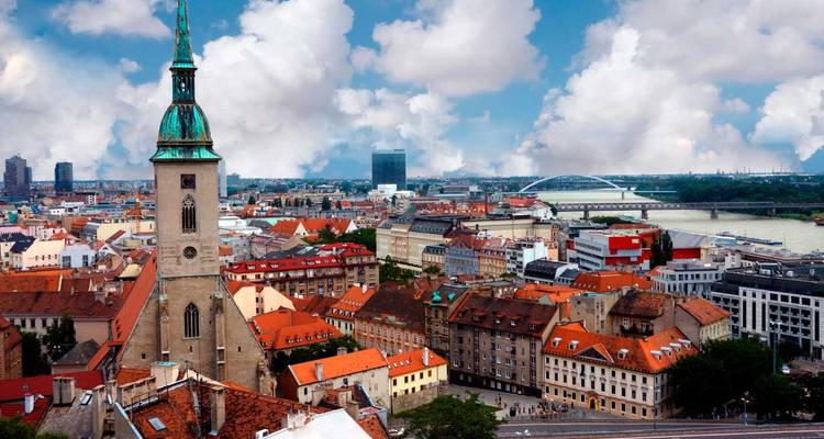 Panorama urbain de Bratislava mettant en vedette la flèche de la Cathédrale Saint-Martin, les bâtiments aux toits rouges et le Danube sous un ciel dégagé avec des nuages duveteux.