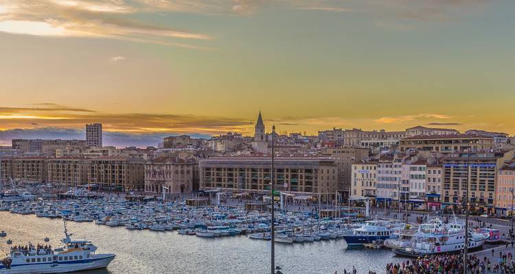 Puesta de sol sobre el Viejo Puerto de Marsella lleno de yates, con el skyline de la ciudad recortado contra un cielo lleno de colores.