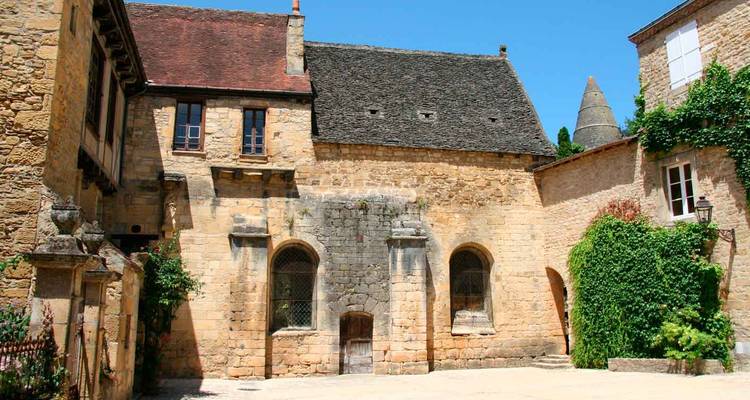 Cour pavée entourée de maisons médiévales jaune ocre avec du lierre dans un village français.